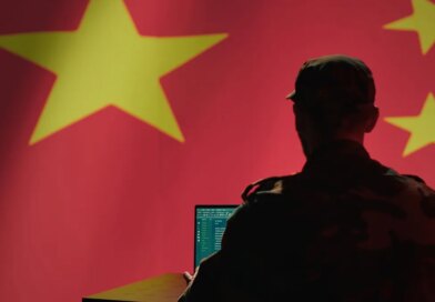A man sits in front of a computer and the Chinese flag.
