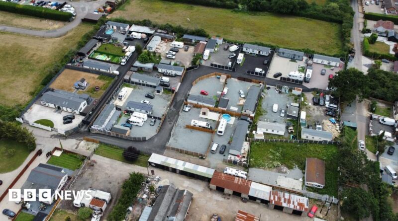An aerial view of lots of caravans and static homes on brownfield land, surrounded by green fields.