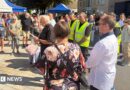 A vicar with lots of people with heads bowed in a town square daytime 