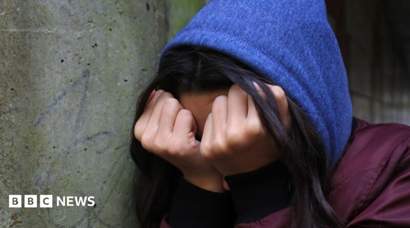 A young person in distress crouches down and covers their face