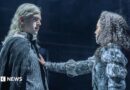 Noah Ritter (Prince Rhaegar Targaryen) and Harmony Rose-Bremner (Lyanna Stark) facing each other in costume in a scene from Game of Thrones: The Mad King. She has an arm outstretched with her palm on his chest