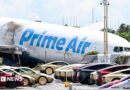 A parking lot filled with Tesla Cybercabs is seen in the foreground as the nose of a Prime Air cargo plane rests on the ground after the aircraft overran the runway and struck cars the previous day at Miami International Airport in Miami, Florida, on September 7, 2026.