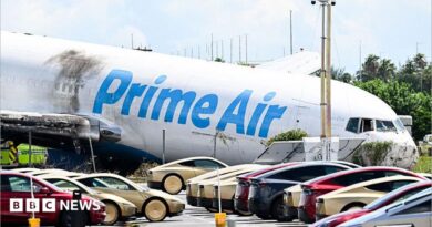 A parking lot filled with Tesla Cybercabs is seen in the foreground as the nose of a Prime Air cargo plane rests on the ground after the aircraft overran the runway and struck cars the previous day at Miami International Airport in Miami, Florida, on September 7, 2026.