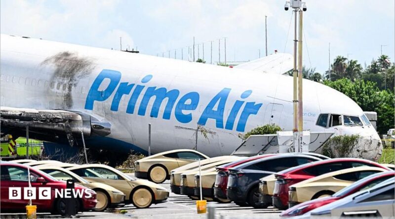A parking lot filled with Tesla Cybercabs is seen in the foreground as the nose of a Prime Air cargo plane rests on the ground after the aircraft overran the runway and struck cars the previous day at Miami International Airport in Miami, Florida, on September 7, 2026.