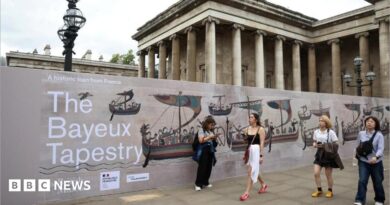 Several people walk past an advertisement for the Bayeux Tapestry at the British Museum in London.