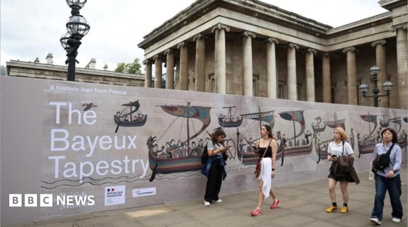 Several people walk past an advertisement for the Bayeux Tapestry at the British Museum in London.