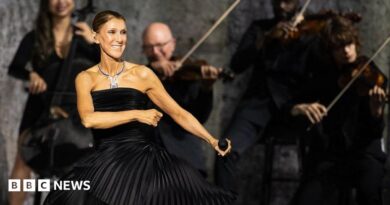 Dion dancing in a black dress, holding a microphone, while musicians play behind her