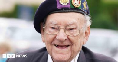 A close-up of Hay, he is smiling and wearing glasses and a uniform