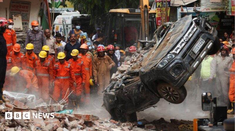 National Disaster Response Force (NDRF) personnel look on at a building collapse in Delhi, while a crushed car is pulled by a digger from the rubble.