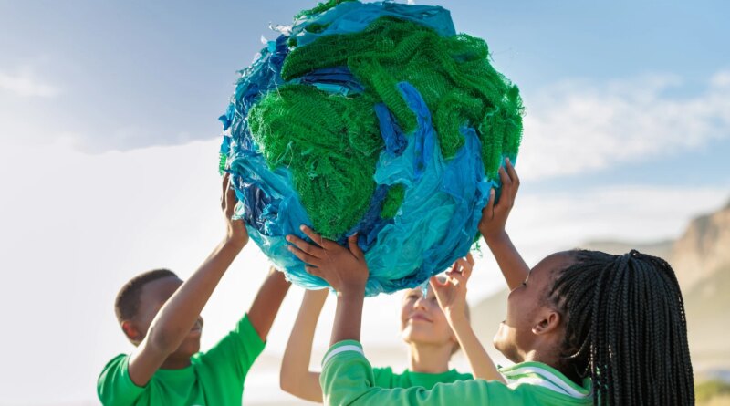 Group of young climate activists holding up a globe together by the sea