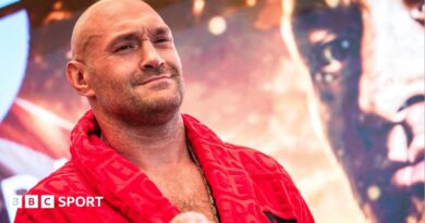 Tyson Fury holds up his hand and is wearing a boxing glove and Anthony Joshua holds up two fingers and has a Union Jack over his shoulders