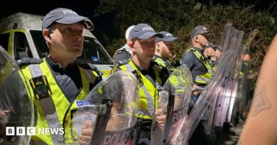 A row of police officers in high vis and holding shields stood facing crowds.