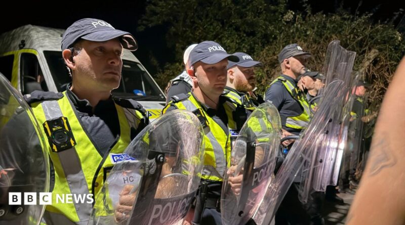 A row of police officers in high vis and holding shields stood facing crowds.