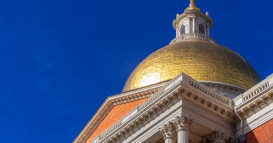 The gold dome of the Massachusetts State House stands against a blue sky.
