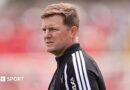 Eddie Howe, wearing a black-and-white tracksuit stop, looks on before a Newcastle match