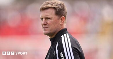 Eddie Howe, wearing a black-and-white tracksuit stop, looks on before a Newcastle match