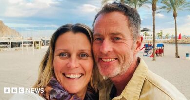 A couple on a beach. It is sunny and the sand is white. Behind them are some trees.