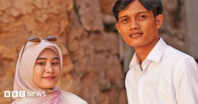 Zia and Yusron smile at the camera - Zia is wearing a dusky pink hijab and has sunglasses on her head, Yusron is wearing an open neck white shirt