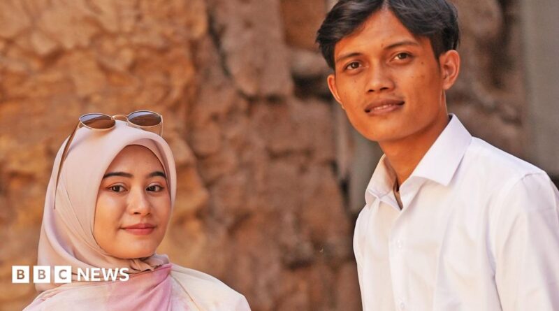 Zia and Yusron smile at the camera - Zia is wearing a dusky pink hijab and has sunglasses on her head, Yusron is wearing an open neck white shirt