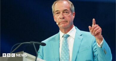 Nigel farage, wearing a light blue suit and white shirt, gestures with his left hand 