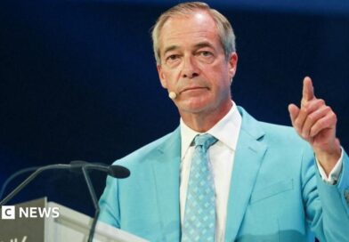 Nigel farage, wearing a light blue suit and white shirt, gestures with his left hand 