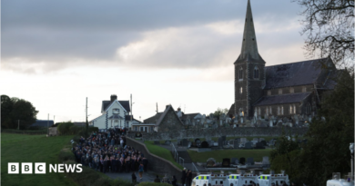 Orange Order members and their supporters gather near Drumcree Parish Church in Portadown. There are white police vehicles further down the road.