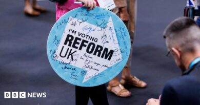 A woman holding a sign saying I'm Voting Reform UK enters the Reform conference. The sign has autographs on it from Reform politicians.
