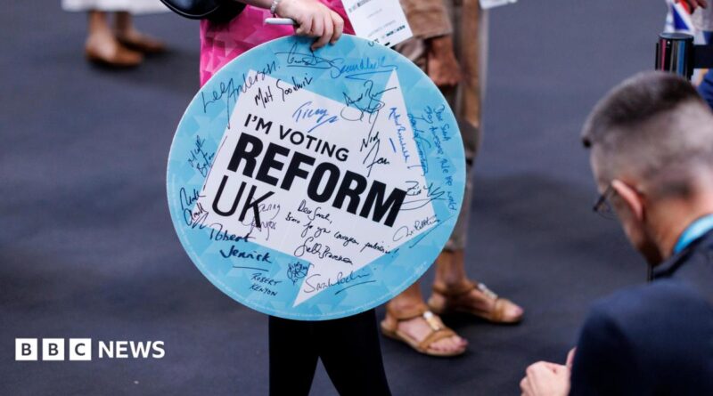 A woman holding a sign saying I'm Voting Reform UK enters the Reform conference. The sign has autographs on it from Reform politicians.