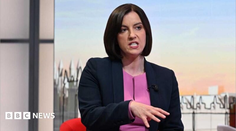 Bridget wears a navy blazer over a purple top sitting and talking in front of the illustrated Sunday with Laura Kuenssberg set.