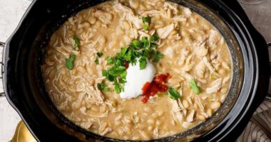Slow cooker filled with white chicken chili topped with cottage cheese, hot sauce, and chopped fresh herbs.