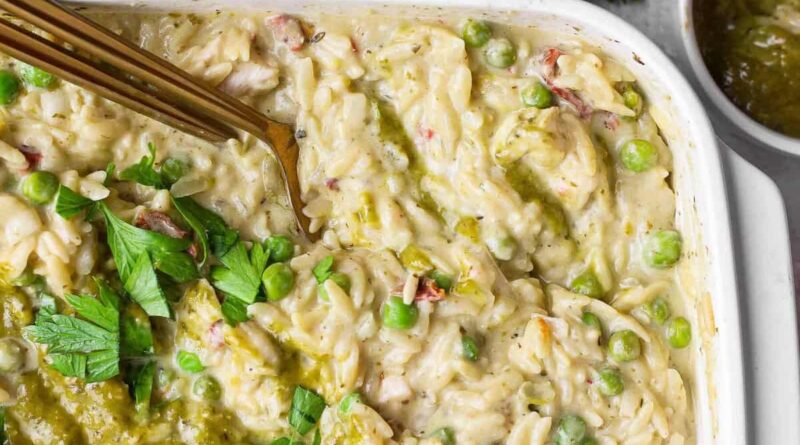 Close-up of creamy chicken pesto orzo with peas, sun-dried tomatoes, pesto, and fresh parsley.