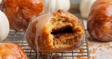 Glazed cottage cheese pumpkin fritter with a bite removed to show the spiced brown sugar center, surrounded by more fritters and small pumpkins.