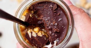 Spoon breaking through the chocolate shell on an individual Snickers cheesecake cup to reveal peanut butter and cottage cheese layers.