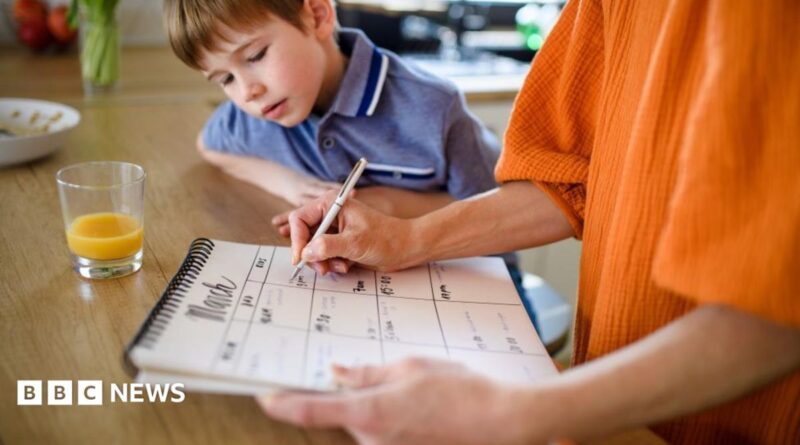 A woman holds a calendar and is writing things down, while a small child peers at the calendar