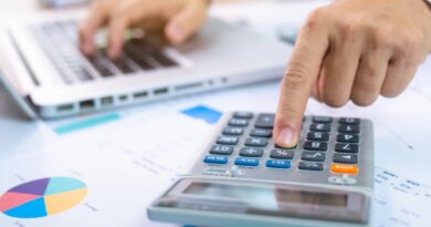 person with one hand typing on a laptop and the other working a calculator