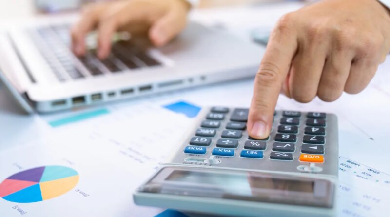 person with one hand typing on a laptop and the other working a calculator