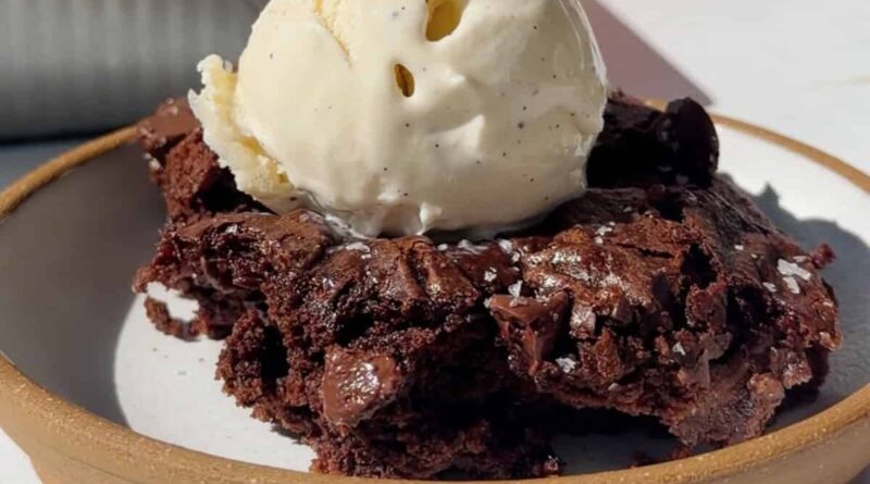 Fudgy cottage cheese brownie topped with a scoop of vanilla ice cream on a ceramic plate.