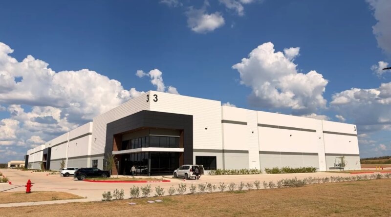 A white warehouse stands against a partly cloudy sky.