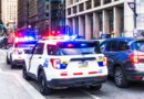 Police vehicles with their lights flashing alongside traffic in downtown Philadelphia.