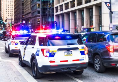 Police vehicles with their lights flashing alongside traffic in downtown Philadelphia.
