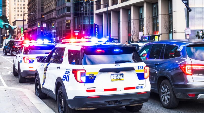 Police vehicles with their lights flashing alongside traffic in downtown Philadelphia.