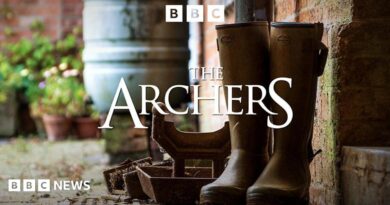 A pair of brown Wellington boots are visible next to a brick wall. The image is emblazoned with the words "The Archers".