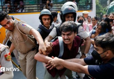 CJP at Jantar Mantar: 'Cockroach' group says leaders detained at Delhi protest A man is being held by men in official uniforms as another man grapples with them. More people are stood behind in pink uniforms holding other protesters.