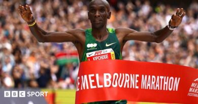Eliud Kipchoge holding his arms aloft as he wins crosses the finish line.