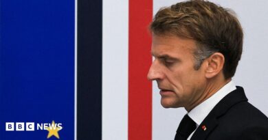 Close up of French President Emmanuel Macron taken from the side. He has short brown hair, and is wearing a white shirt, black jacket and tie.