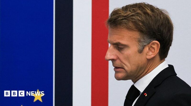 Close up of French President Emmanuel Macron taken from the side. He has short brown hair, and is wearing a white shirt, black jacket and tie.