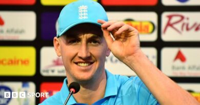 Harry Brook, wearing a blue cap, looks straight ahead while half-smiling in front of a microphone