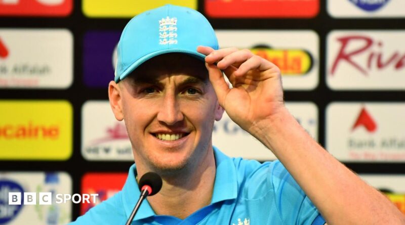 Harry Brook, wearing a blue cap, looks straight ahead while half-smiling in front of a microphone