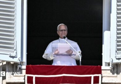 Pope Leo XIV delivering the Sunday Angelus prayer from the balcony of his residence overlooking St Peter's Square. He's in the traditional white cassock, mozzetta cape and zucchetto silk hat over his head.